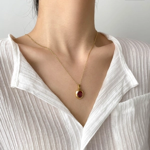 Detail of a vintage gold necklace with oval ruby pendant worn over a white pleated shirt