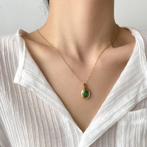 Elegant emerald pendant necklace with gold chain worn by a model on a white shirt