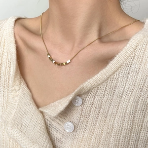 Gold cube necklace with snake chain worn by a model against a cream knit background