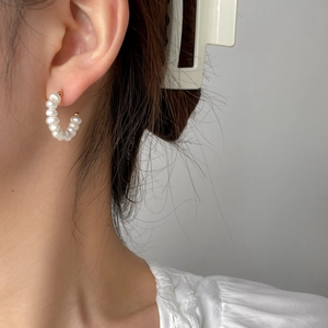 Close-up of a model wearing C-shaped irregular pearl earrings with golden metal details