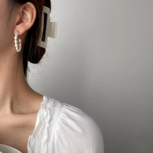 Close-up of handmade baroque pearl hoop earrings on a model wearing a white ruffled top