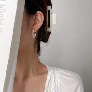 Detail of a C-shaped handmade pearl earring on model with white round pearls