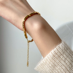 Detail of a minimalist gold geometric cube bracelet on a wrist with a soft sweater