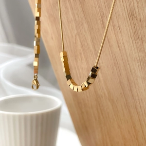 Macro detail of geometric cube pendant on gold snake chain hanging on wood stand