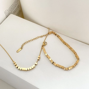 Detail shot of 18K gold geometric cube necklace and bracelet set with K18 engraving