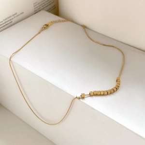 Detailed close-up of golden geometric cube beads on a sleek snake chain necklace