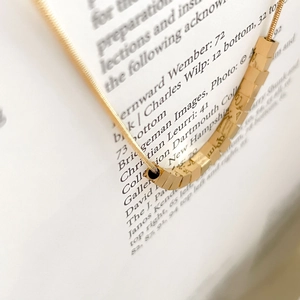Macro detail of minimalist gold geometric square pendant on a sleek snake chain necklace