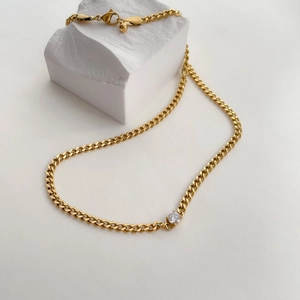 Close-up of golden Cuban link necklace with white zircon pendant on a white stone block
