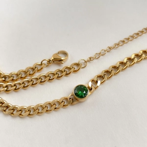 Detailed close-up of golden Cuban link necklace with bezel-set green stone and lobster clasp