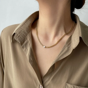 Close-up of golden Cuban chain necklace with a single round white zircon on model