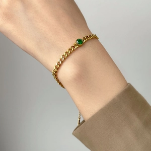 Detail of a gold Cuban link chain bracelet with a round green gemstone on a wrist