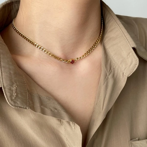 Close-up of elegant gold Cuban chain necklace with a round red zircon on a female model