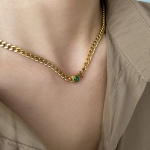 Detail of a gold Cuban link chain necklace with a centered green oval zircon gemstone
