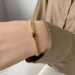 Close-up of elegant gold chain bracelet with a deep red zircon stone on a wrist