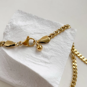 Close-up of golden Cuban link chain with a lobster clasp and ball pendant detail