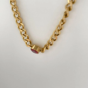 Macro view of gold chain link necklace featuring a round red gemstone pendant detail