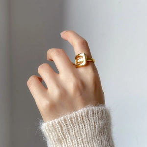 Close-up of gold geometric hollow ring on finger with soft knit sweater sleeve
