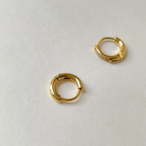 Dettaglio macro degli orecchini huggie dorati con piccoli zirconi e chiusura a molla