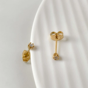Dettaglio di orecchini a lobo minimalisti in oro con zircone tondo e chiusura a farfalla