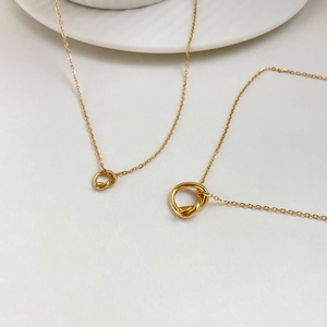 Detail shot of two gold-tone knotted necklaces with intertwined rings on O-chains