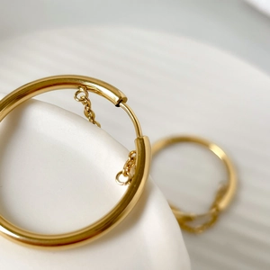 Macro shot of gold hoop earrings featuring unique inner chain details on a ceramic base