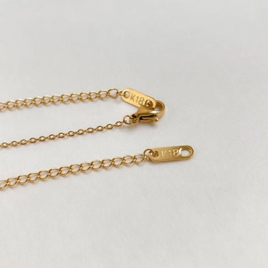 Close-up of gold knotted chain necklace with K18 engraved tag and lobster clasp detail