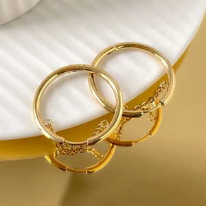 Close-up of gold chain tassel hoop earrings resting on a textured ceramic surface
