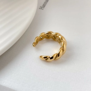 Detail of gold-plated twisted rope ring with high-polish finish on minimalist background