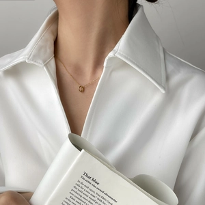 Close-up of a minimalist gold knot pendant necklace worn on a white shirt