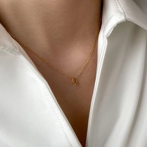 Detail of minimalist gold knotted pendant necklace worn on neck with white shirt