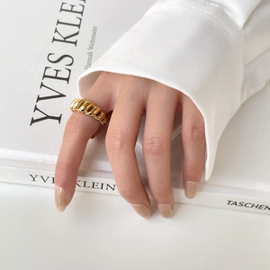 Close-up of a gold twisted dome croissant ring worn on a finger with elegant white background