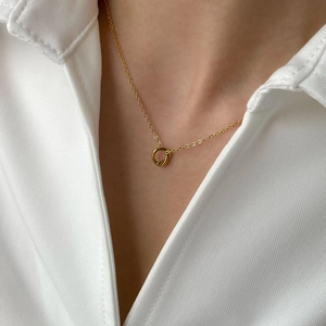 Close-up of a double-ring knotted pendant on a fine gold chain with white shirt background