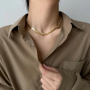 Close-up of golden herringbone chain necklace with twisted weave on a female neck