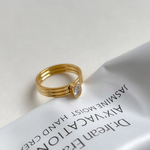 Détail d'une bague dorée à trois anneaux ornée d'une pierre de zircone ovale brillante