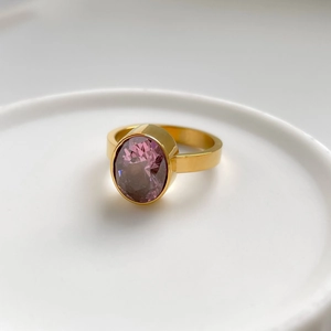 Détail d'une bague dorée ornée d'un grand zircon violet ovale avec serti clos chic