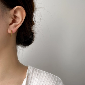 Gros plan d'une boucle d'oreille barre verticale en or au style minimaliste épuré