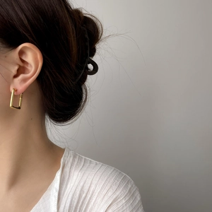 Boucles d'oreilles créoles rectangulaires dorées minimalistes portées par un mannequin