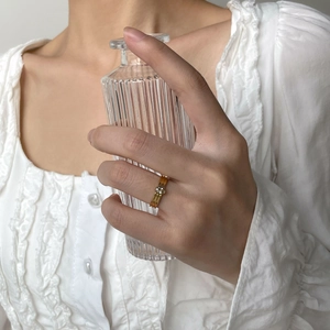 Détail d'une bague tressée dorée minimaliste avec zircon rond, portée par un mannequin en lumière