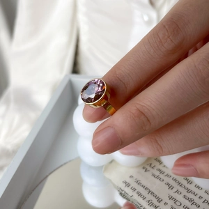 Détail d'une bague dorée avec un grand zircon violet ovale portée à la main