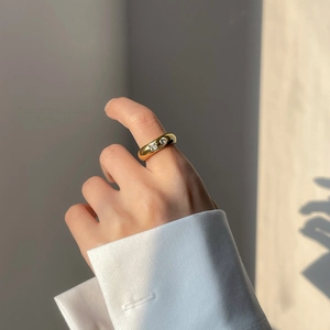 Détail d'une bague dorée épaisse avec oxydes de zirconium carrés et ronds sur le doigt