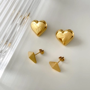 Detail view of gold-plated heart and geometric triangle stud earrings on white surface