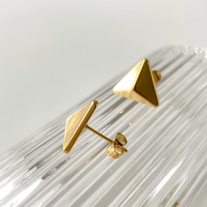 Macro detail of gold-plated triangle stud earrings featuring brushed and polished textures