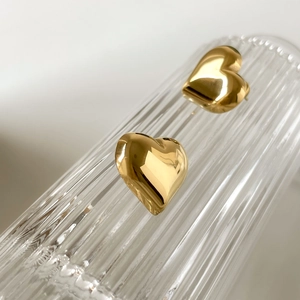Polished 3D gold heart stud earrings displayed on elegant fluted glass texture