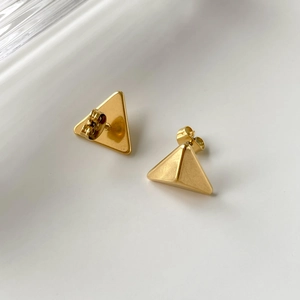 Detail of minimalist gold triangle stud earrings with polished metallic surface finish