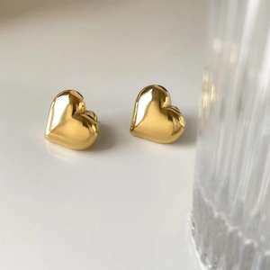 Close-up of polished gold heart stud earrings with a glossy metallic mirror finish