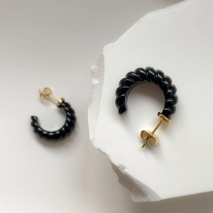 Gros plan de boucles d'oreilles créoles spirales noires sur base en pierre blanche