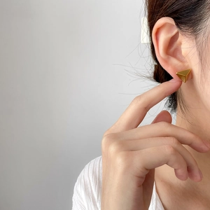 Close-up of a model wearing minimalist polished gold triangular geometric stud earrings