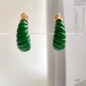 Détail des boucles d'oreilles torsadées en émail vert avec clous dorés sur support acrylique