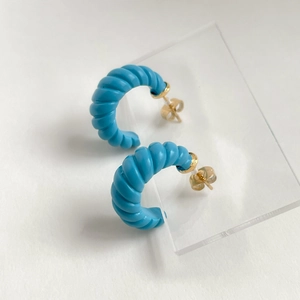 Détail de boucles d'oreilles créoles bleues torsadées avec accents dorés sur support