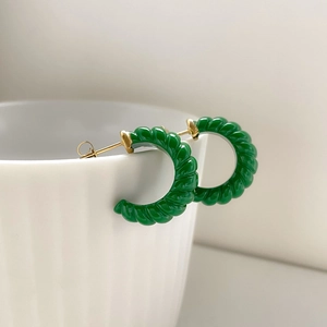 Détail macro de boucles d'oreilles créoles torsadées vertes sur un bord de tasse